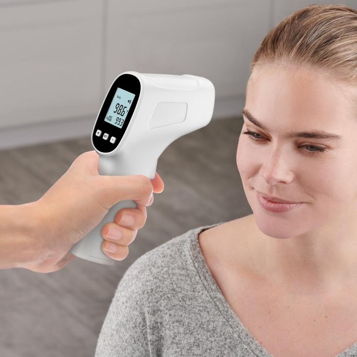 Person using a digital thermometer on a woman's forehead with a blurred background